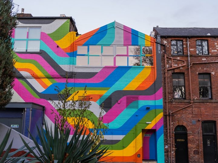 Lush green field with a distant house and trees under a blue sky.