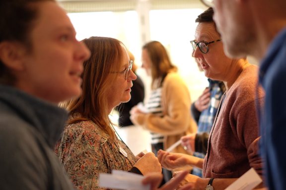 A group of people engaged in a conversation, holding papers and interacting closely.