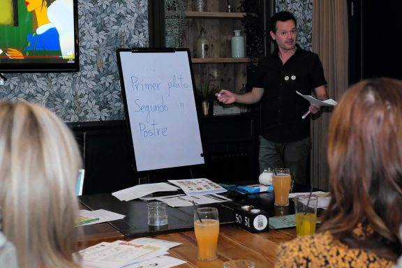 A speaker presenting to an audience with a flipchart and drinks on the table.