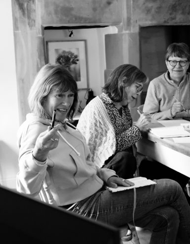 A group of three people engaged in a creative activity, with one woman smiling and gesturing.
