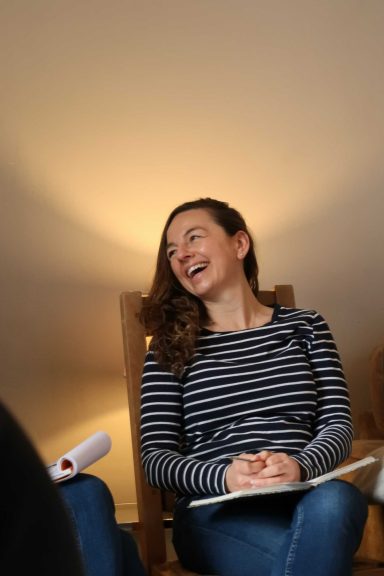 Woman in a striped top smiling, seated, with a warm light background.