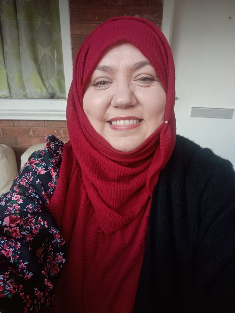 Smiling woman wearing a red hijab and a floral-patterned sleeve top.