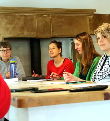 Four people engaged in a discussion around a table, with notes and drinks visible.