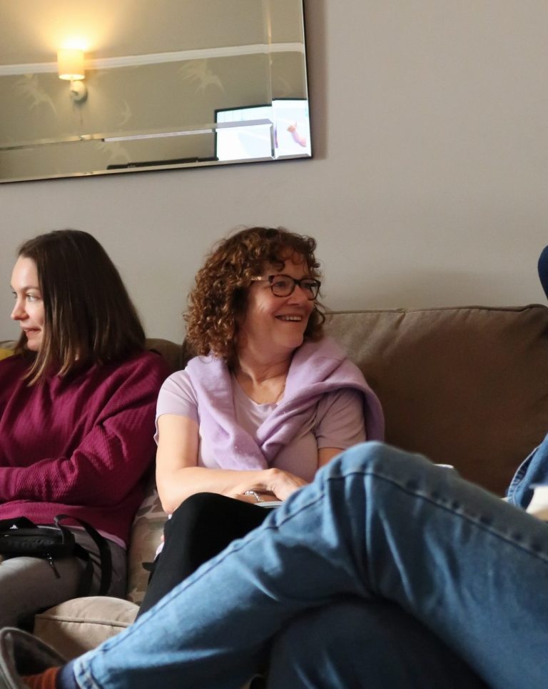 Three people sitting on a sofa, smiling and engaged in conversation.