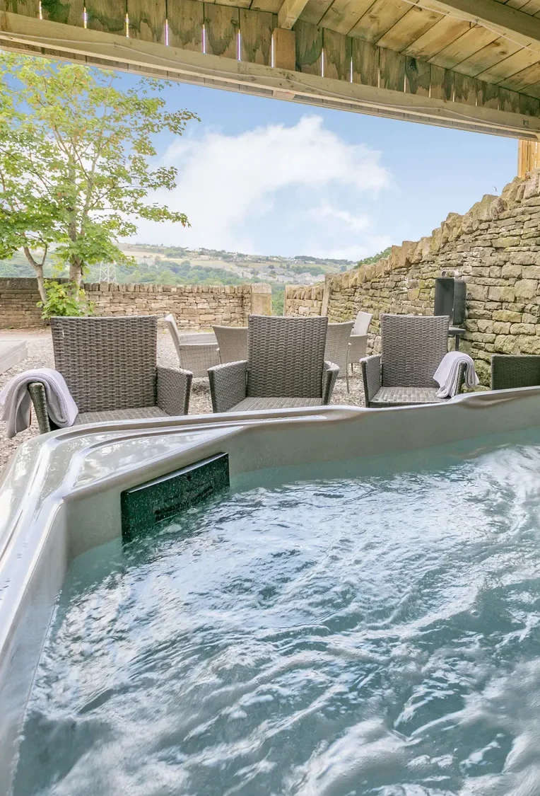 Hot tub with bubbling water under a wooden shelter, surrounded by outdoor seating.