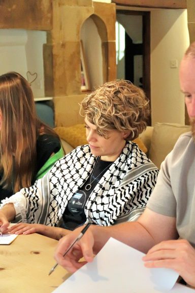 Three individuals seated at a table, writing with focused expressions.