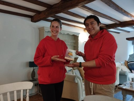 Two people in red hoodies smile while holding a trophy in a cozy, well-lit room.