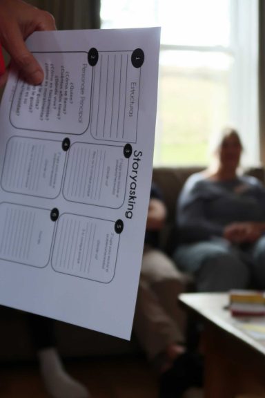 A person holding a paper form in front of two seated individuals in a living room.
