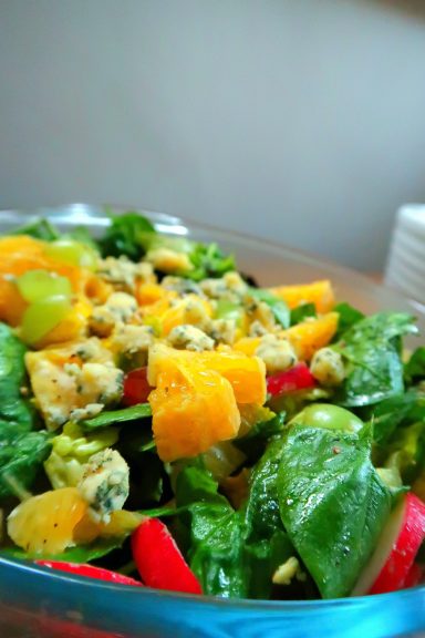 A fresh salad with mixed greens, colourful fruits, nuts, and a light dressing.