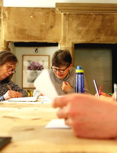 Two people engaged in a creative activity at a table, with sketches and materials nearby.