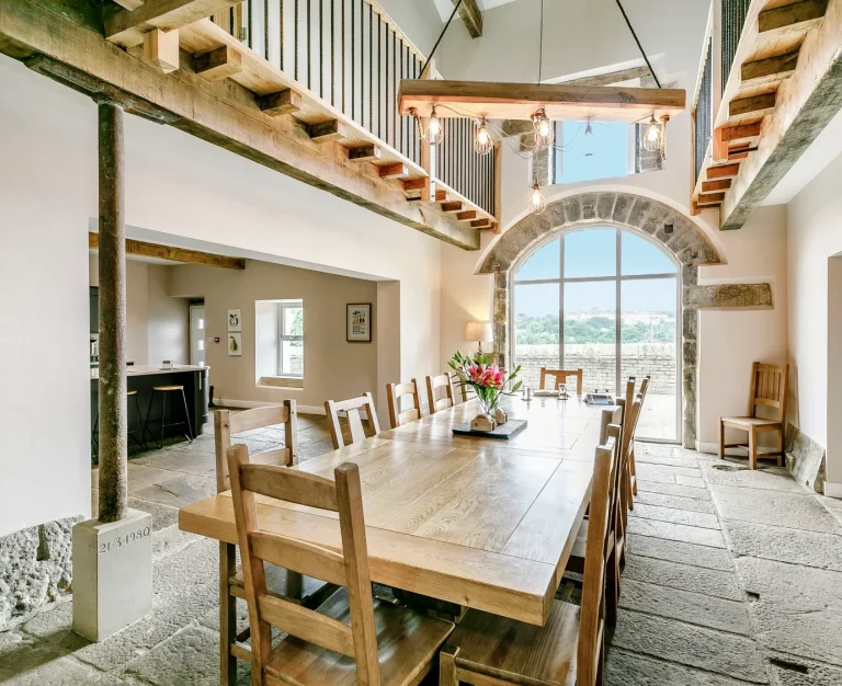 Bright dining area with a long wooden table, chairs, and large window overlooking countryside.