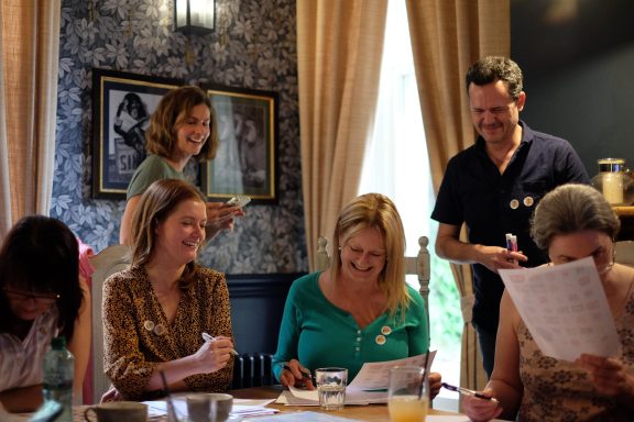 A group of women and a man engaged in a lively discussion around a table.