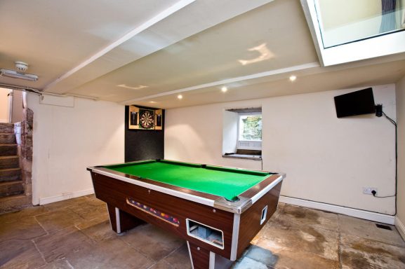 A billiard table with a green felt surface in a well-lit basement room.