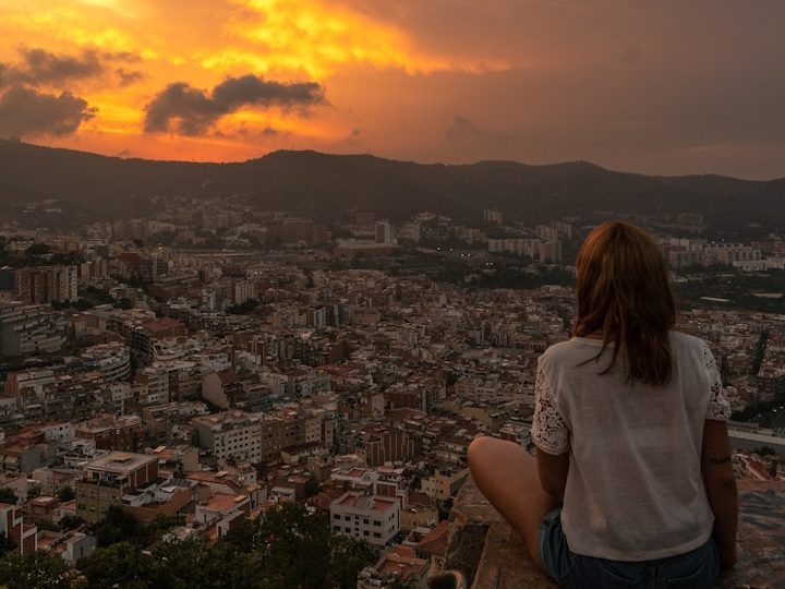 Lush green field with a distant house and trees under a blue sky.