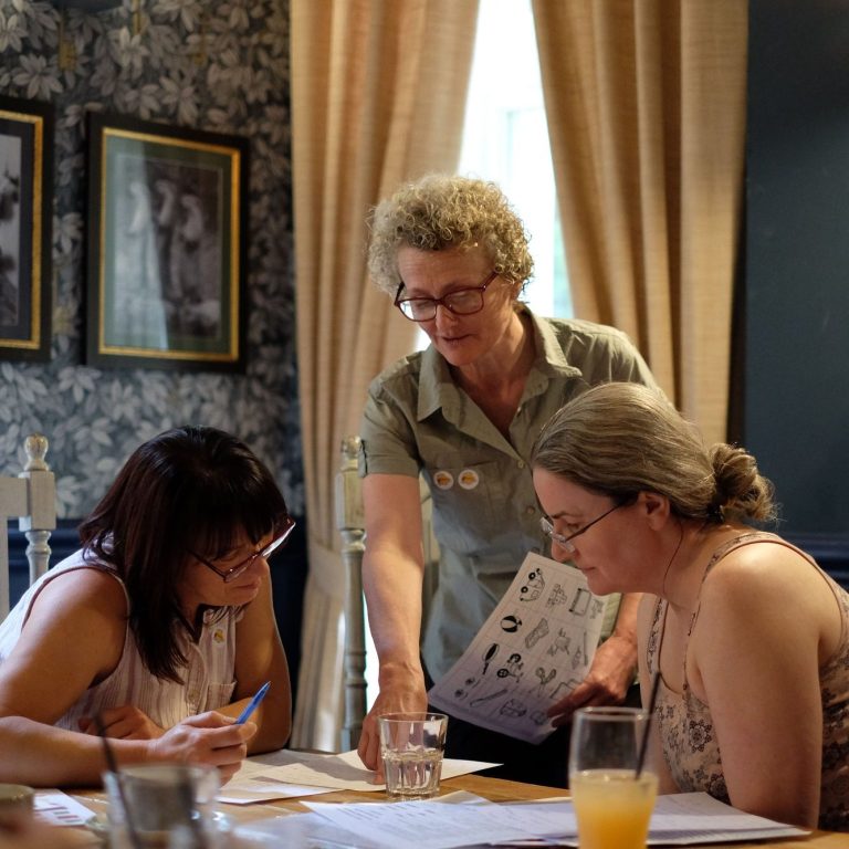 Outdoor seating area with wooden picnic tables, surrounded by green hills under a cloudy sky.