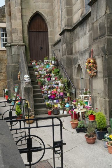 Colourful flowers and potted plants line a stone staircase next to a church entrance.