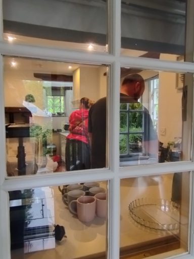 People preparing food in a kitchen, seen through a window.