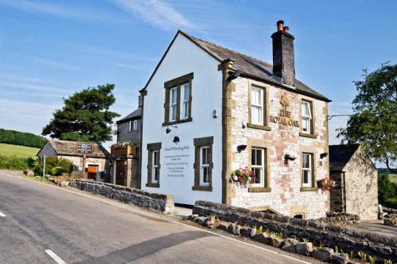 Two-storey stone house with white walls, set beside a country road.