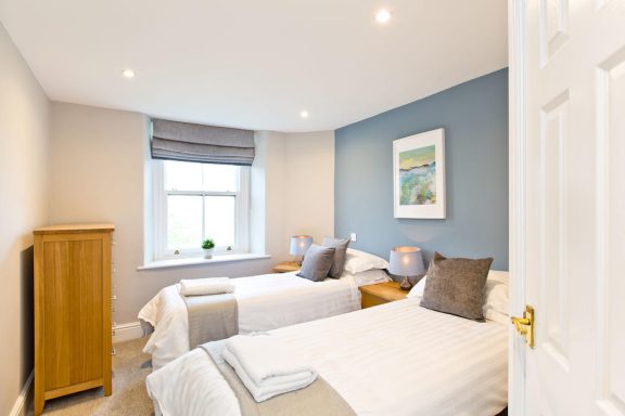 Bright bedroom with two single beds, light decor, and a window with blinds.