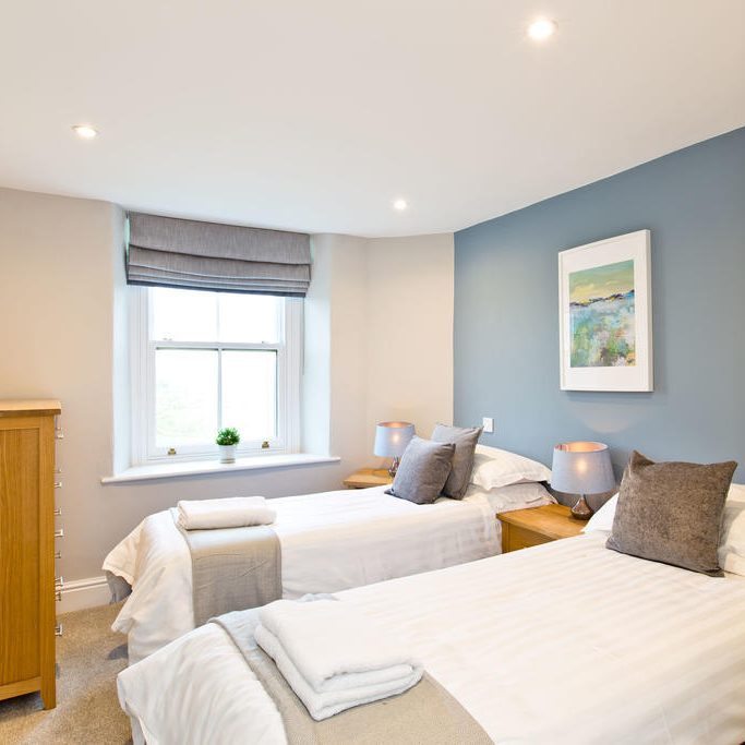 Spanish Holiday Course in Bakewell Bright bedroom featuring two single beds, a dresser, and a window with soft furnishings.