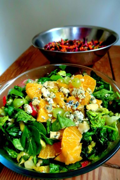 A colourful salad with greens, orange slices, and blue cheese, with a second bowl of mixed fruit.