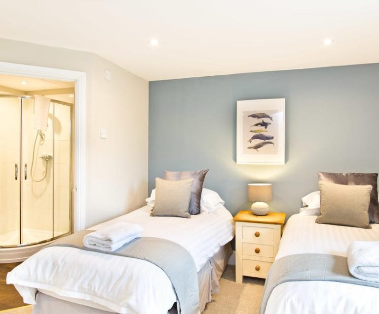 A bright bedroom with two single beds, a shower enclosure, and soft decor.