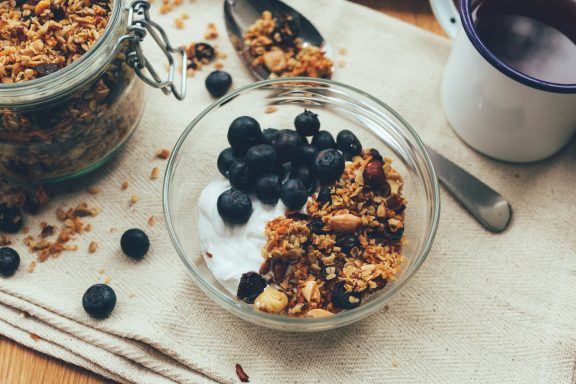 Bowl of yogurt topped with granola, blueberries, and scattered nuts.