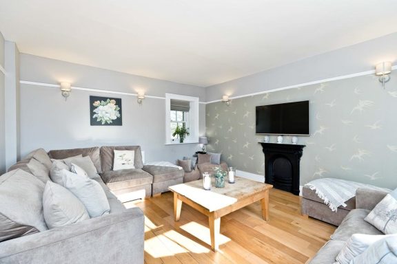 Modern living room with grey walls, a TV, plush sofas, and a wooden coffee table.